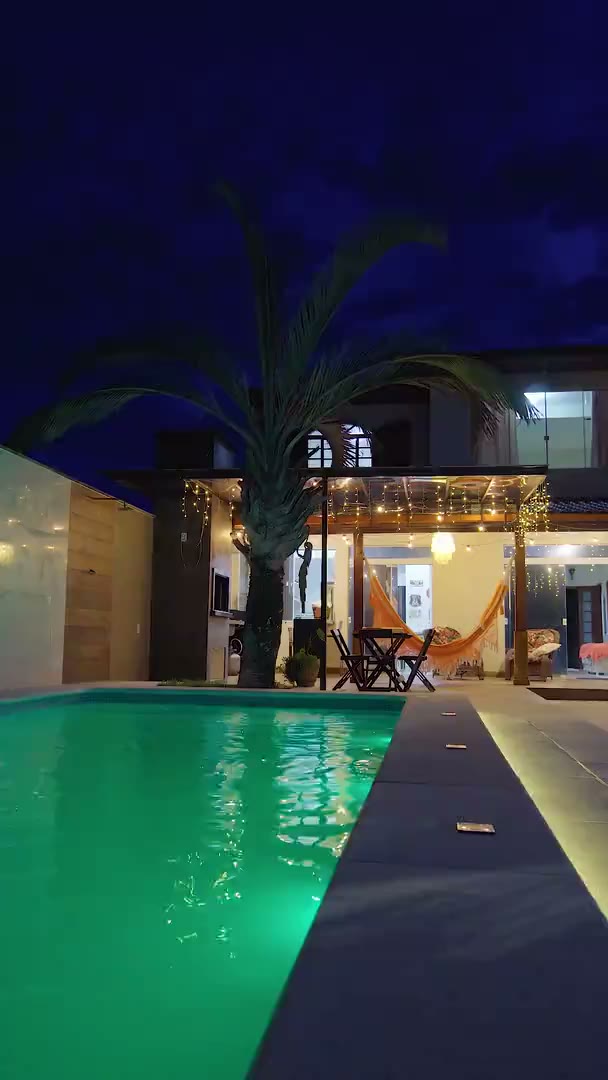 A casa à noite, com a varanda acesa e a piscina iluminada, e depois vista de cima